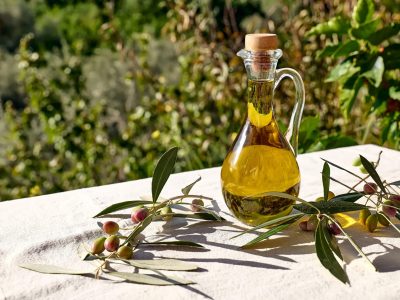 Extra virgin olive oil and olive branch in the bottle on the table with linen tablecloth in the olive grove. Healthy mediterranean food.